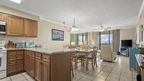 A spacious kitchen with wooden cabinets, a central island, and a dining area with chairs and a table. - White Sands and Good Times (Orange Beach)
