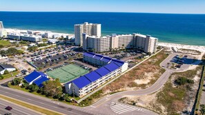 A coastal hotel with multiple buildings, a parking lot, and a tennis court. - White Sands and Good Times (Orange Beach)