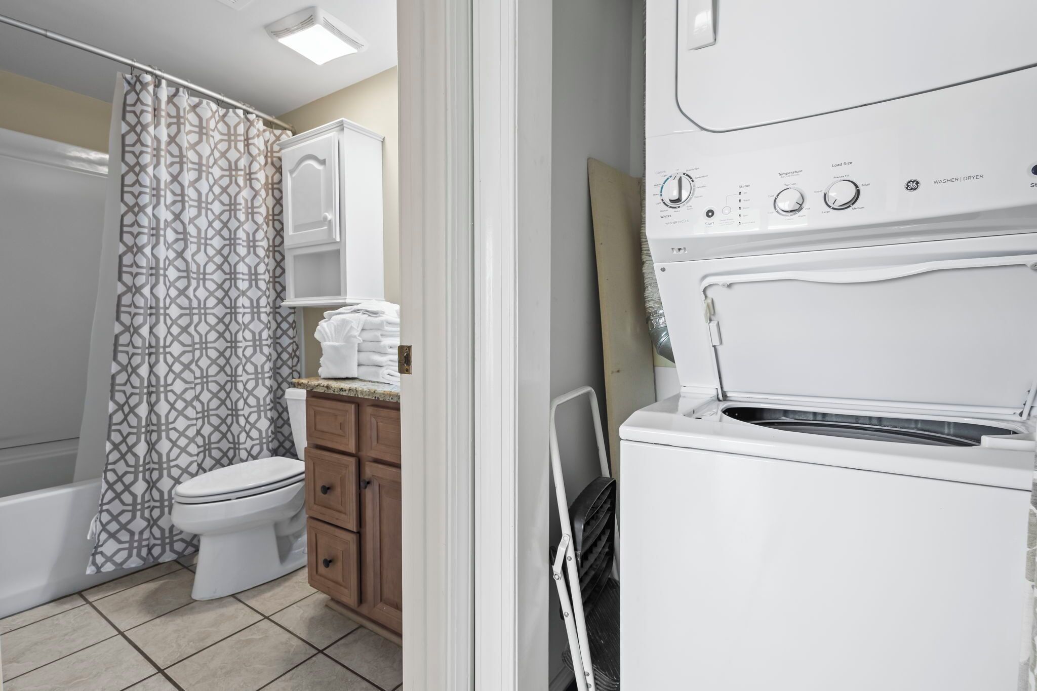 A bathroom with a toilet, a shower curtain, a cabinet, and a washing machine.