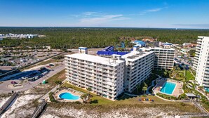 A multi-story hotel with a pool, surrounded by a parking lot and a beach area. - White Sands and Good Times (Orange Beach)