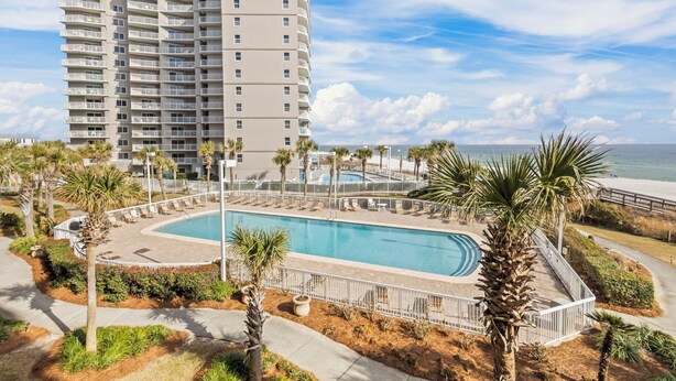 A high-rise hotel with a swimming pool surrounded by palm trees and a view of the ocean. - White Sands and Good Times (Orange Beach)