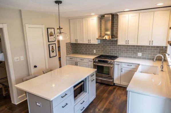 A modern kitchen with white cabinets, a central island, a built-in oven, and a stainless steel range hood.