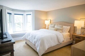 A bedroom with a bed, bedside lamps, a desk, and a window with curtains.