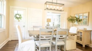 Un comedor con una mesa de madera y sillas blancas, un candelabro y una puerta decorada con un adorno navideño.