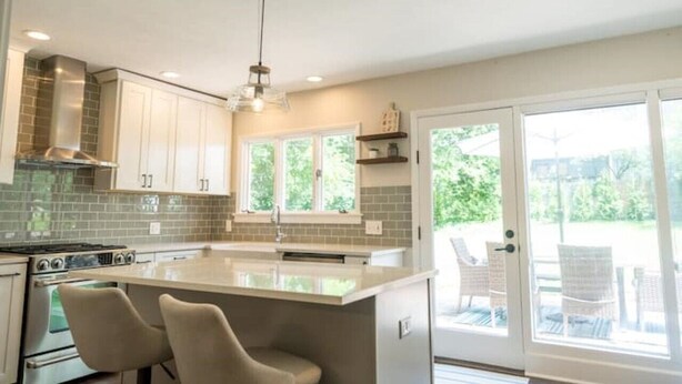 Una cocina moderna con una isla grande, armarios blancos y vistas al exterior a través de una puerta corrediza de vidrio.
