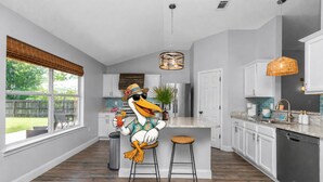 A modern kitchen with a large island, white cabinetry, and a view of the backyard. - Celebrate Mother`s Day on the Beach (Navarre)
