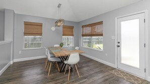 A room with a wooden dining table, white chairs, and a door with a frosted glass panel. - Celebrate Mother`s Day on the Beach (Navarre)