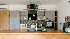 Eine moderne Küche mit Holzarbeitsplatte, eingebauten Geräten, Pendelleuchten und einer gemusterten Spritzschutzwand.