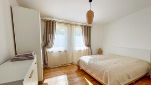 Ein Schlafzimmer mit Bett, Schminktisch, Fenster mit Vorhängen und einer Pendelleuchte.
