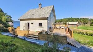 A white wooden house with a sloped roof, a deck, and a small outdoor seating area.
