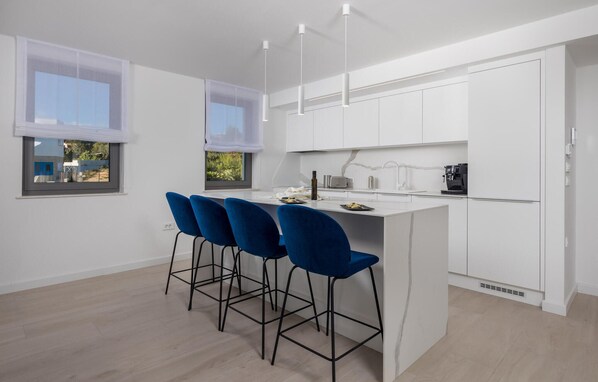 A modern kitchen with white cabinets, a central island with bar stools, and pendant lighting. - 3 bedroom cozy apartment in Krk (Krk)