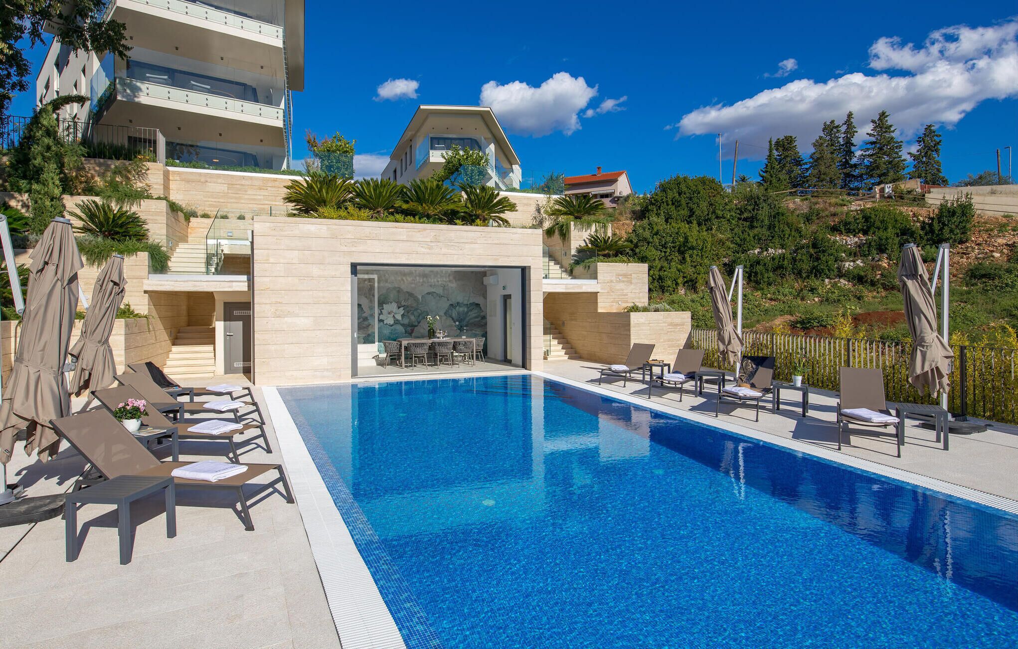 A modern hotel with a swimming pool, lounge chairs, and a dining area.