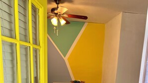 Ein Zimmer mit gelber Tür, Deckenventilator, Tisch mit Stühlen und geometrischem Wandmuster.