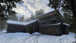 Une maison à deux étages, dont le toit et l’allée sont recouverts de neige, et qui est entourée de grands arbres.