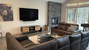 Un salon moderne avec une cheminée en pierre, des canapés en cuir et un téléviseur à écran plat fixé au mur.