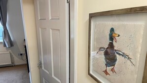 Una habitación con una puerta que da a otro espacio, una obra de arte enmarcada de un pato en la pared y un radiador.