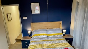 Una cama bien hecha con ropa de cama estampada y dos toallas rojas, un cabecero de madera, lámparas de noche y una mesita pequeña.