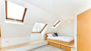Ein Schlafzimmer mit Schlafpodest, Dachfenstern und einem Holzschrank.