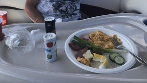 Une personne assise dans un bateau, avec un plateau de repas devant elle, comprenant une assiette avec de la nourriture et des boissons.
