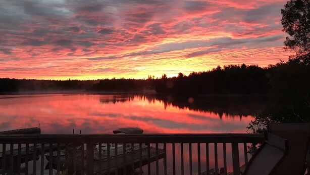 Un coucher de soleil sur un lac paisible, avec un quai en bois et des bateaux.