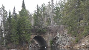 Une rivière paisible, avec une canne à pêche au premier plan et un pont de pierre en arrière-plan.
