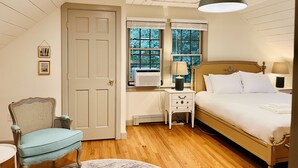 A bedroom with a wooden ceiling, a bed with white bedding, a nightstand with a lamp, a chair, and a window with blinds. - Private Cape Cod Cottage. Walk to Ellis Landing Beach! (Brewster)