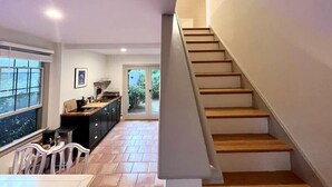A modern kitchen with a dining area, a staircase, and a view through a glass door. - Private Cape Cod Cottage. Walk to Ellis Landing Beach! (Brewster)