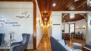 Un pasillo con piso de madera, un sillón tapizado de color gris, un sofá azul y una pared con un letrero que dice 'Galveston Island'.