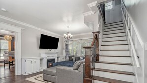 Ein großzügiges Wohnzimmer mit einem großen, grauen Ecksofa, einem Kamin und einer Treppe mit Holzwangen.