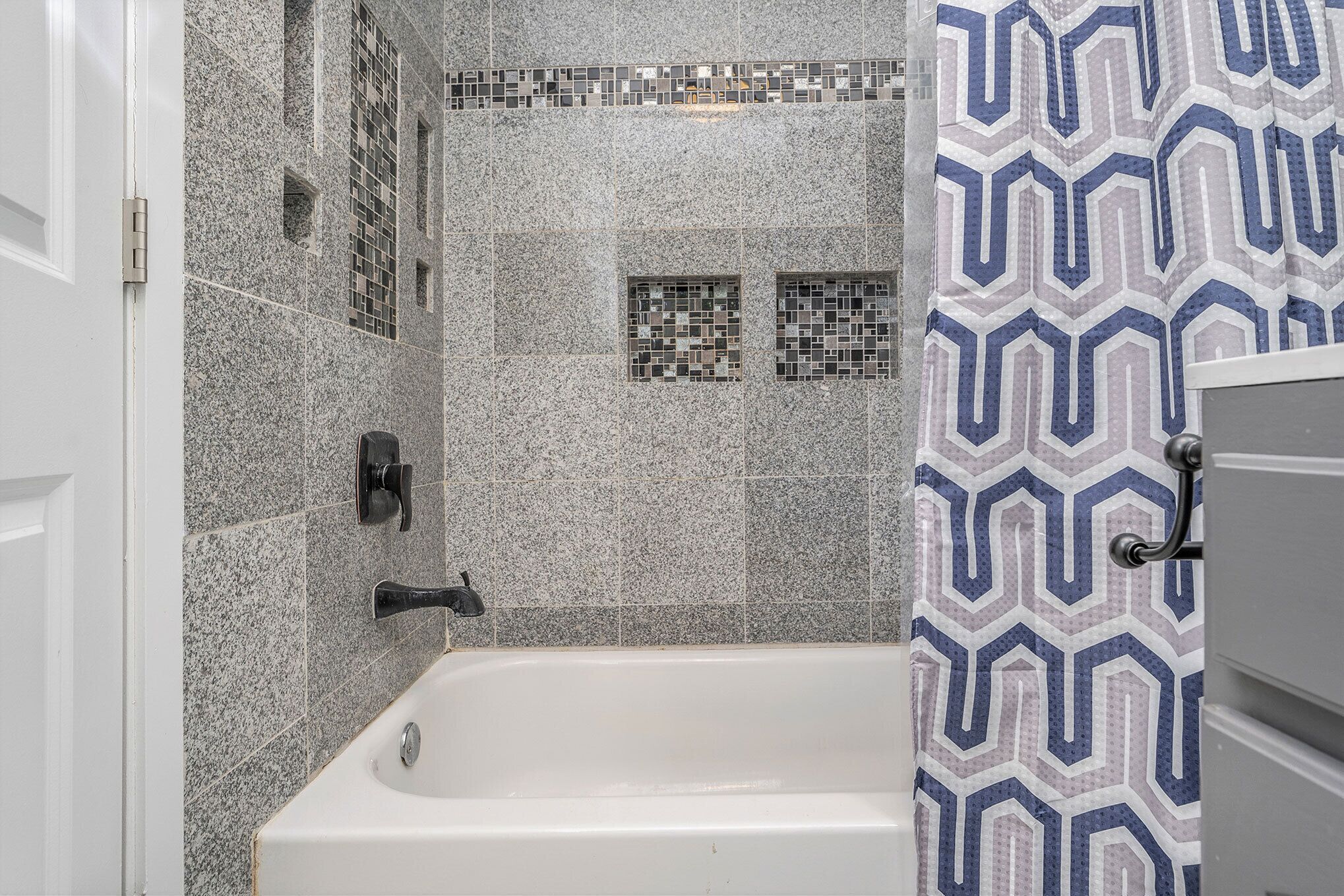 Un baño con una bañera blanca, paredes con azulejos y una cortina de ducha estampada.