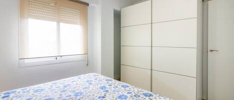 A bedroom with a bed, a window with blinds, and a wardrobe.