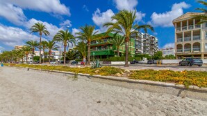 Un hotel frente a la playa con varios pisos, palmeras y una playa de arena.