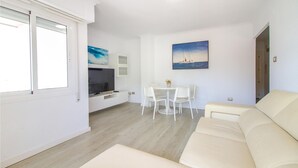 Una sala moderna con un sofá beige, una mesa de comedor con sillas, un televisor de pantalla plana y obras de arte en las paredes.