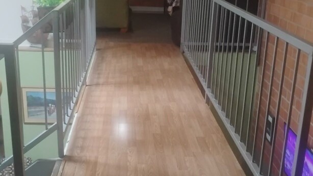 A corridor with wooden flooring, metal railings, and a staircase.
