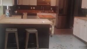 A kitchen with a central island, stools, cabinets, a refrigerator, and a hanging light fixture.