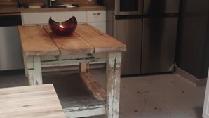 A kitchen with a wooden table, a metal bowl, and a refrigerator.
