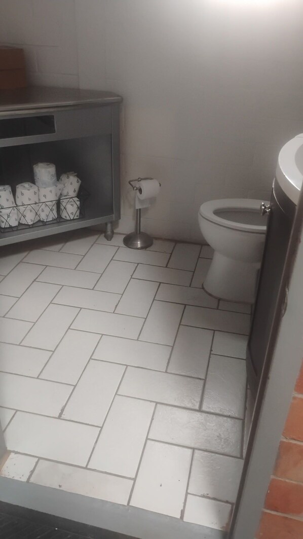 Un baño con inodoro, un dispensador de papel higiénico y una repisa con rollos de papel.