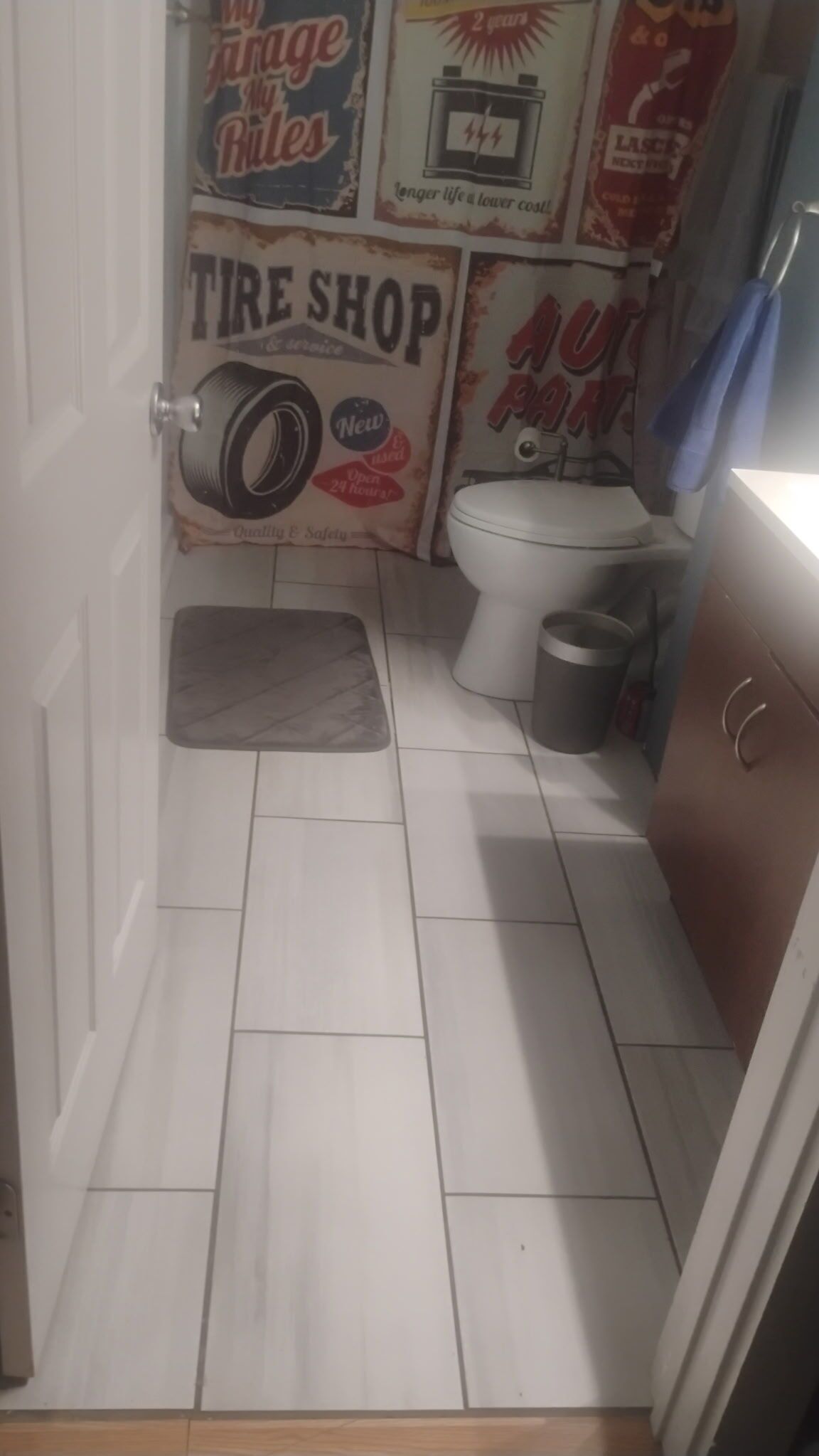 A small bathroom with a toilet, a trash bin, a rug, and a door with a sign.
