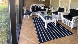 A covered patio with wicker furniture, a glass table, and a black and white striped rug. - Inviting farmhouse with private pool (Oxford)