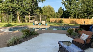 A backyard with a swimming pool, a patio with a glass-top table and wicker chairs, and a wooden fence. - Inviting farmhouse with private pool (Oxford)