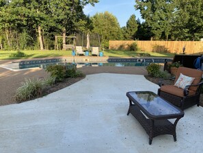 A backyard with a swimming pool, a patio with a glass-top table and wicker chairs, and a wooden fence. - Inviting farmhouse with private pool (Oxford)
