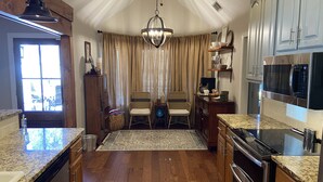 A kitchen with wooden cabinets, a built-in oven, a microwave, and a dining area with two wicker chairs and a rug. - Inviting farmhouse with private pool (Oxford)