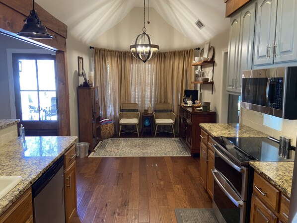 A kitchen with wooden cabinets, a built-in oven, a microwave, and a dining area with two wicker chairs and a rug. - Inviting farmhouse with private pool (Oxford)
