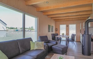 Een moderne woonkamer met een bank, stoelen, een eettafel en een keuken met een koelkast.