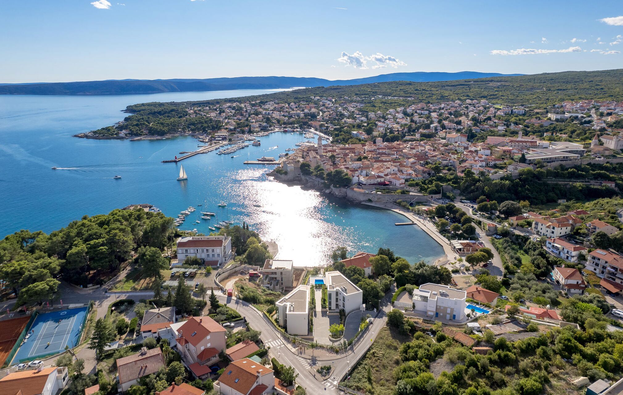 An aerial view of a coastal town with a marina, residential buildings, and a prominent church.