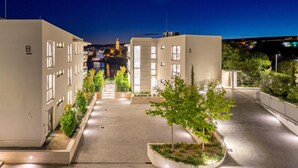 En modern byggnad med en central innergård, omgiven av träd och med fönster som lyser upp omgivningen.