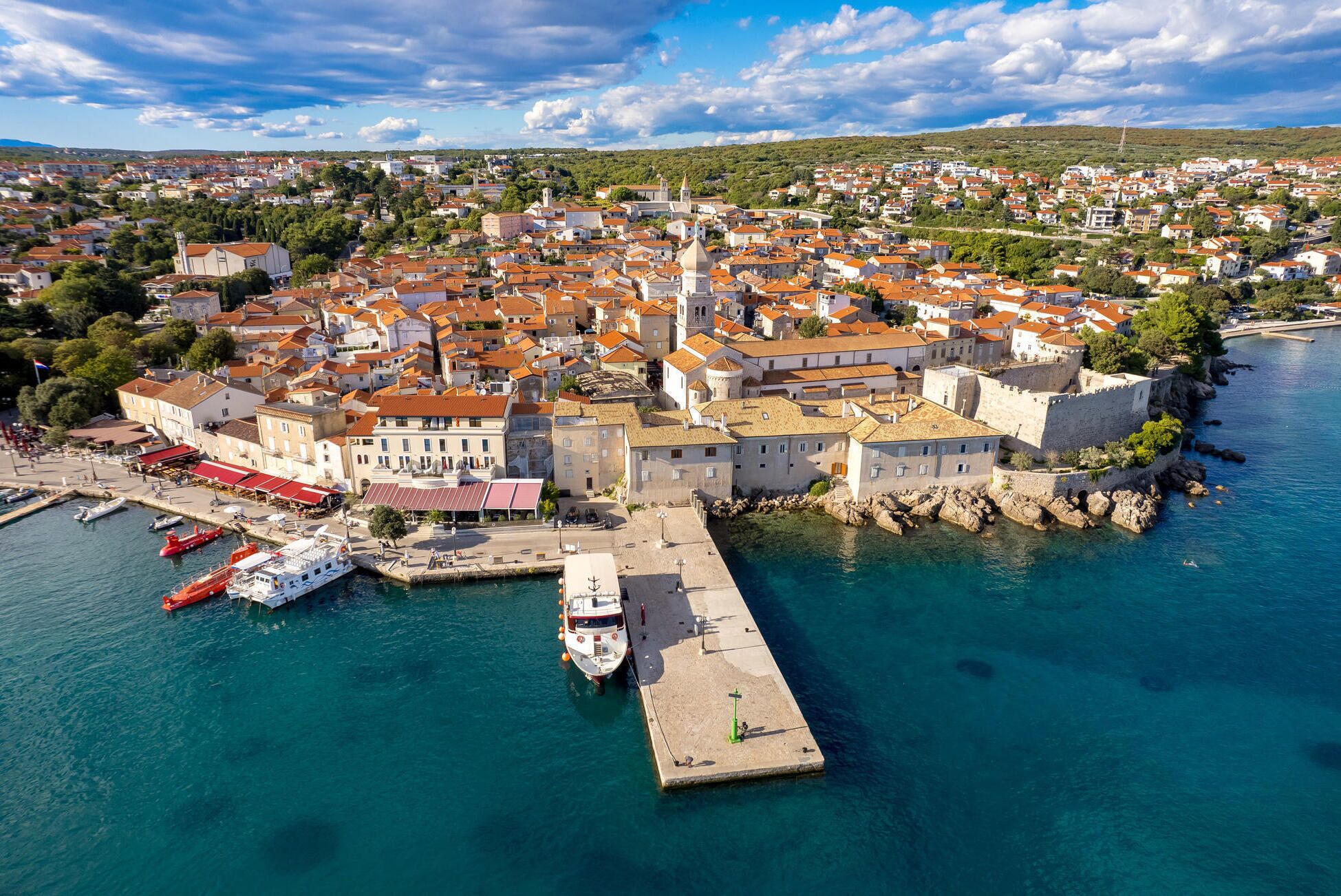 An aerial view of a coastal town with historic buildings, a harbor with boats, and a prominent church tower.