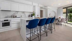 A modern kitchen with white cabinets, a marble backsplash, and a central island with blue bar stools. - 3 bedroom beach front apartment in Krk (Krk)