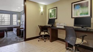 Hotellihuone, jossa on työpöytä, kaksi tuolia, tietokone ja suuri ikkuna.