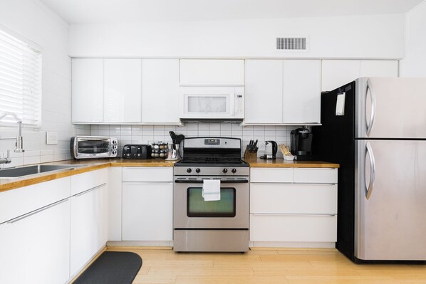 Une cuisine moderne avec des meubles blancs, une cuisinière en acier inoxydable, un four à micro-ondes, un grille-pain et un réfrigérateur.